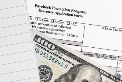 A $100 US bill sitting on top of a US government document titled "Paycheck Protection Program."