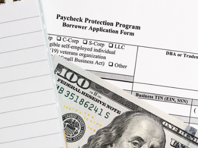 A $100 US bill sitting on top of a US government document titled "Paycheck Protection Program."