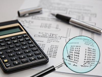 A calculator and pen on top of a tax form with a magnifying glass magnifying some of the numbers and the total.