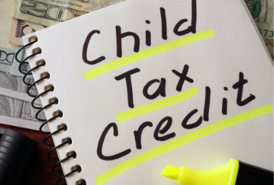 A notepad with "Child Tax Credit" written in black ink and highlighted, sitting on top of a pile of American currency.