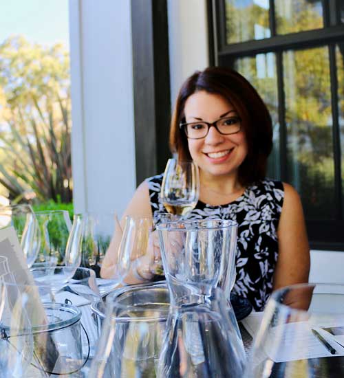 Leah Belanger holding a wine glass outside in front of table of wine glasses