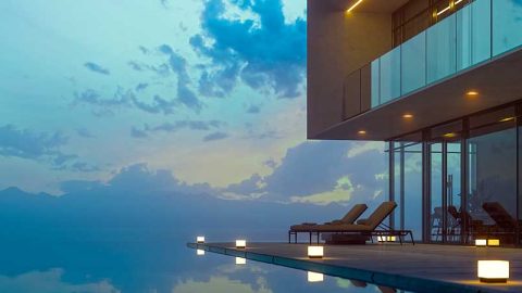 The exterior view of a modern home, its pool and two lounge chairs at dusk.