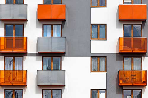 A modern apartment building with orange, translucent orange, and gray balconies.