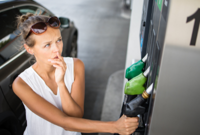 A Caucasian woman standing at a gas pump looking perplexed.