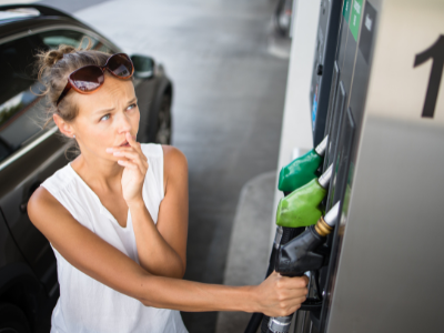 A Caucasian woman standing at a gas pump looking perplexed.