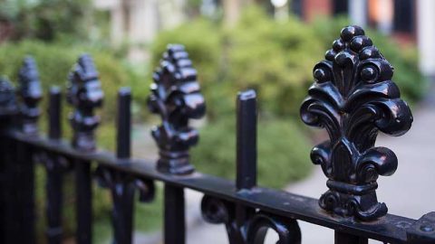A close up of the top of a black wrought iron fence with decorative fluer de lis toppers.